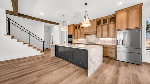 kitchen featuring stainless steel appliances, a sink, light wood-type flooring, tasteful backsplash, and an island with sink