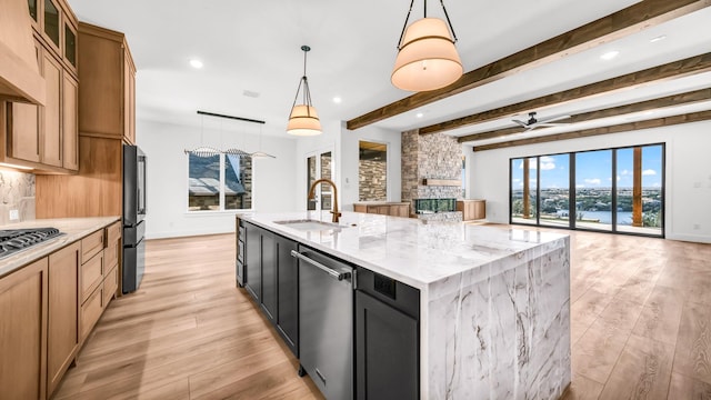 kitchen featuring a center island with sink, ceiling fan, open floor plan, light stone countertops, and a sink