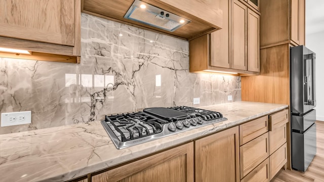 kitchen with light stone counters, stainless steel gas cooktop, decorative backsplash, light wood-style floors, and high end black fridge