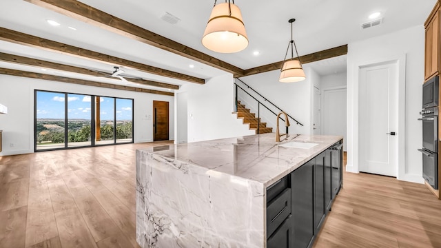 kitchen with light wood finished floors, open floor plan, a sink, and beamed ceiling