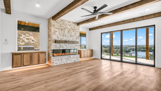 unfurnished living room featuring visible vents, ceiling fan, a stone fireplace, wood finished floors, and beamed ceiling