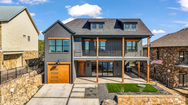 back of house featuring brick siding, a patio, a shingled roof, board and batten siding, and a balcony