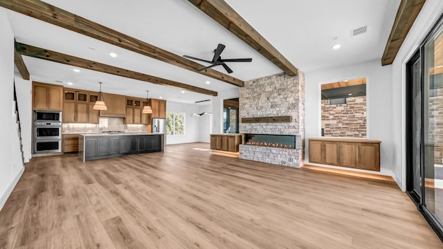 unfurnished living room with a stone fireplace, sink, light hardwood / wood-style flooring, ceiling fan, and beam ceiling