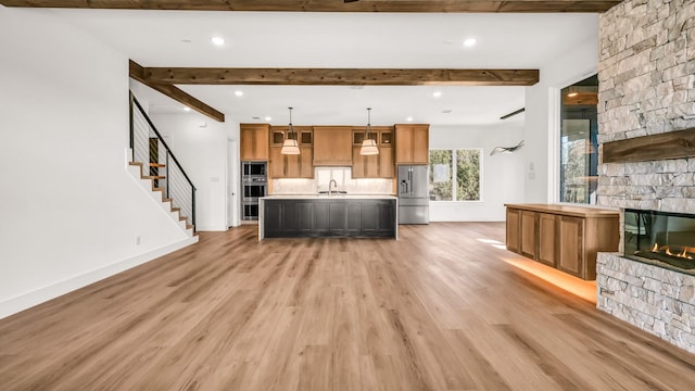 unfurnished living room with light wood-style flooring, a fireplace, a sink, baseboards, and beamed ceiling