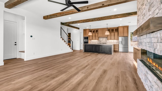 unfurnished living room with a sink, stairs, a stone fireplace, light wood-type flooring, and beam ceiling