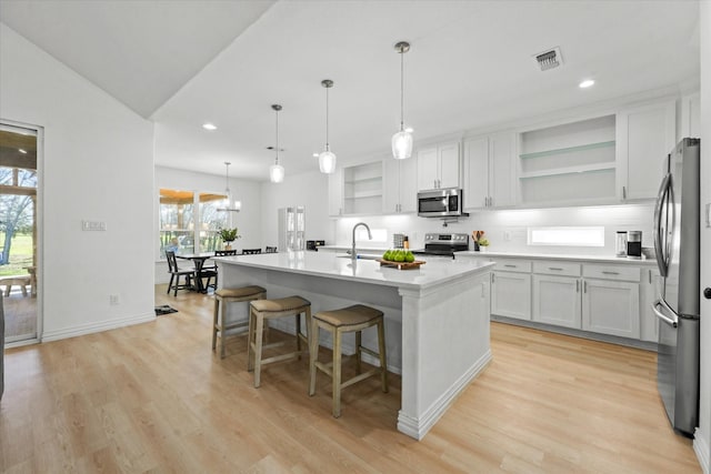 kitchen featuring stainless steel appliances, a kitchen island with sink, sink, decorative light fixtures, and white cabinets