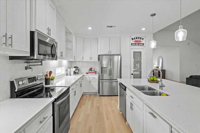 kitchen with sink, tasteful backsplash, pendant lighting, white cabinets, and appliances with stainless steel finishes