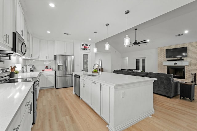 kitchen with white cabinets, stainless steel appliances, a brick fireplace, and an island with sink