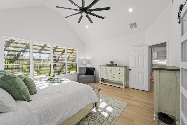 bedroom with a barn door, ceiling fan, high vaulted ceiling, and light hardwood / wood-style floors