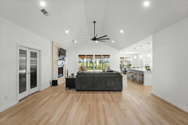 living room featuring a fireplace, light hardwood / wood-style floors, high vaulted ceiling, and ceiling fan