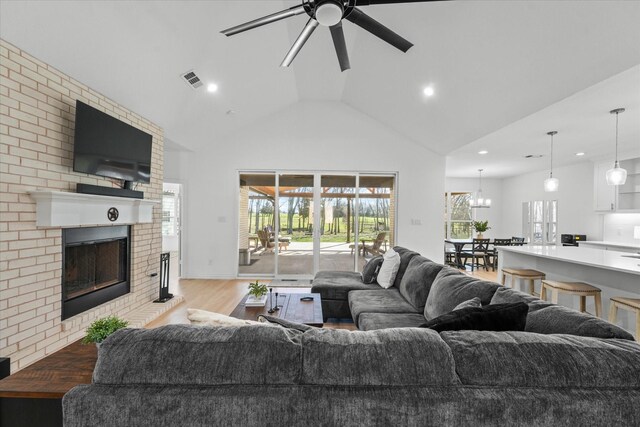 living room with ceiling fan, a fireplace, lofted ceiling, and light hardwood / wood-style flooring