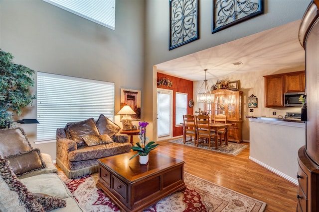 living area with an inviting chandelier, a high ceiling, baseboards, and wood finished floors