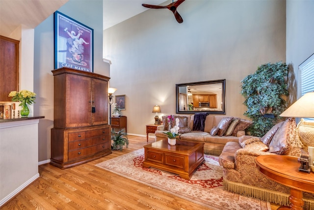 living area featuring a towering ceiling, ceiling fan, baseboards, and wood finished floors