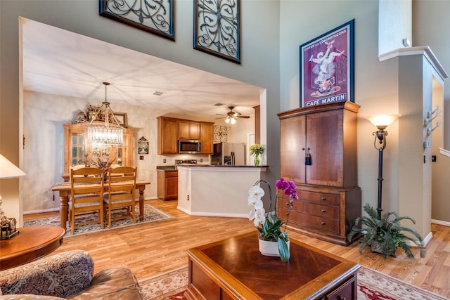 living area featuring ceiling fan with notable chandelier, light wood finished floors, a towering ceiling, and baseboards