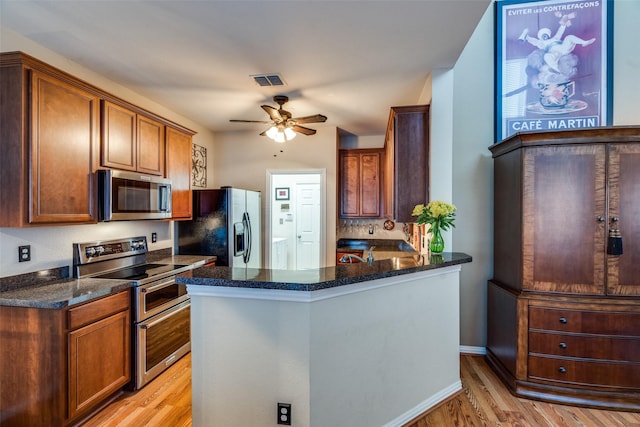 kitchen featuring dark stone counters, a ceiling fan, appliances with stainless steel finishes, a peninsula, and light wood-type flooring