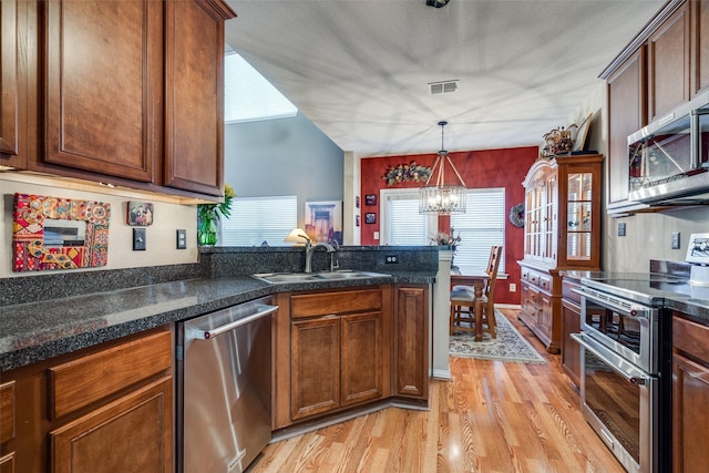 kitchen featuring a chandelier, light wood-style flooring, a sink, appliances with stainless steel finishes, and decorative light fixtures