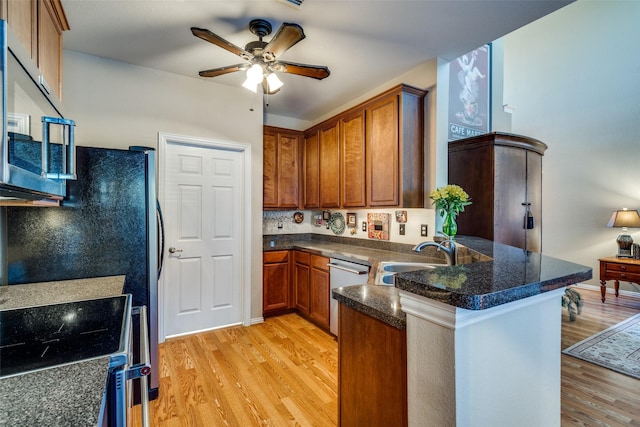 kitchen featuring appliances with stainless steel finishes, light wood-style floors, brown cabinetry, a sink, and a peninsula