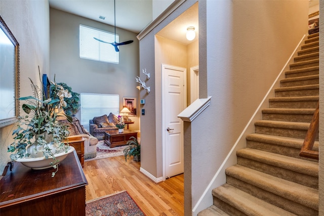 stairs featuring ceiling fan, a high ceiling, wood finished floors, and baseboards