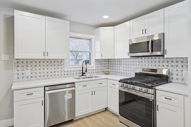 kitchen featuring sink, appliances with stainless steel finishes, backsplash, white cabinets, and light wood-type flooring