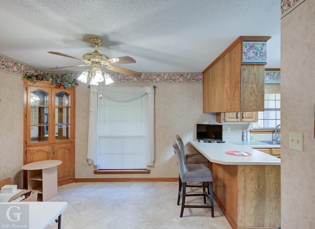 kitchen featuring sink, ceiling fan, a textured ceiling, kitchen peninsula, and a breakfast bar area