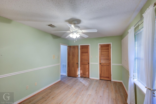 unfurnished bedroom with multiple closets, ceiling fan, a textured ceiling, and light wood-type flooring