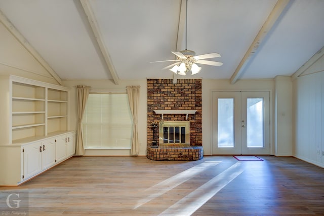 unfurnished living room with ceiling fan, french doors, a brick fireplace, lofted ceiling with beams, and light hardwood / wood-style floors