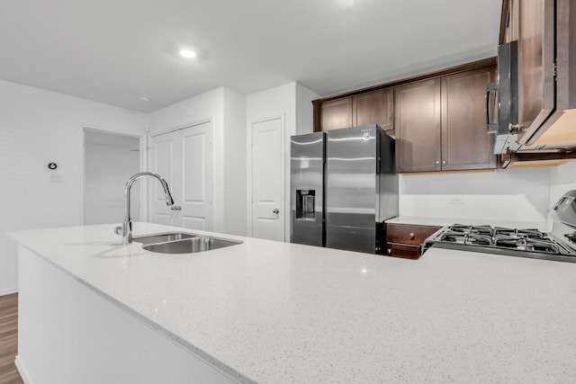 kitchen with stainless steel refrigerator with ice dispenser, stove, light stone counters, sink, and hardwood / wood-style floors