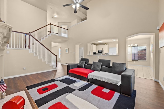 living room featuring a high ceiling, ceiling fan with notable chandelier, and wood-type flooring