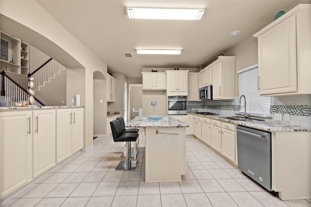 kitchen with a center island, sink, a kitchen breakfast bar, light stone counters, and appliances with stainless steel finishes