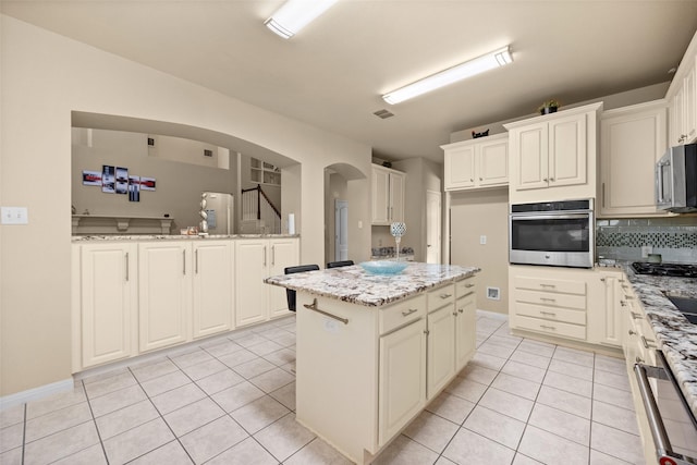 kitchen featuring light tile patterned flooring, a kitchen island, light stone counters, white cabinetry, and stainless steel appliances