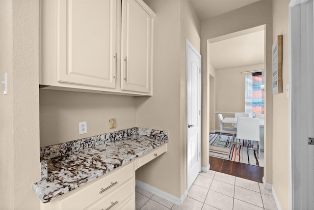 kitchen with white cabinetry, light stone counters, light tile patterned floors, and built in desk