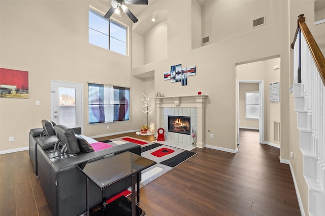 living room featuring ceiling fan, a towering ceiling, dark wood-type flooring, and a tiled fireplace