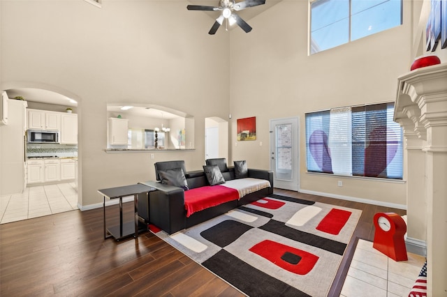 living room featuring ceiling fan with notable chandelier, dark hardwood / wood-style floors, and a high ceiling