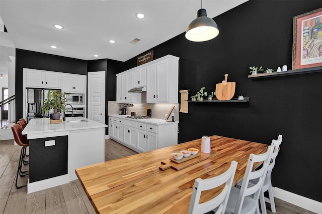 kitchen featuring stainless steel appliances, white cabinetry, hanging light fixtures, and a kitchen island with sink