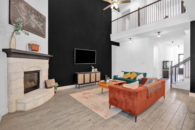 living room featuring a fireplace, a towering ceiling, light hardwood / wood-style floors, and ceiling fan