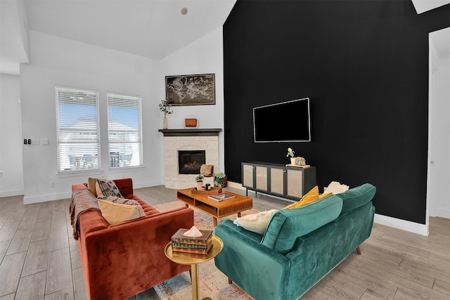 living room with high vaulted ceiling, light hardwood / wood-style flooring, and a stone fireplace