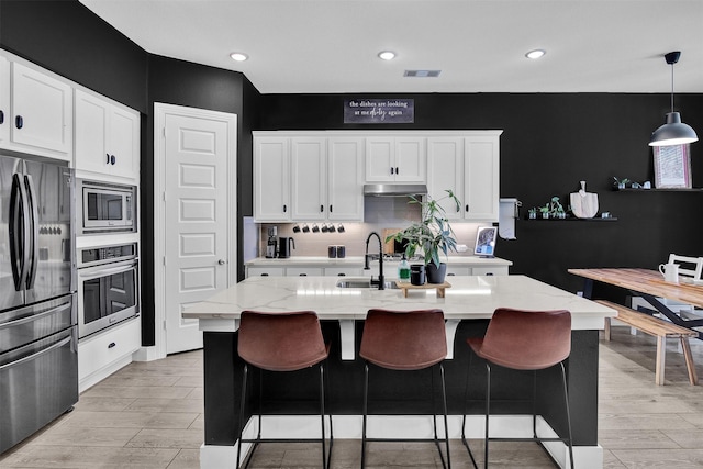 kitchen with a kitchen island with sink, white cabinets, pendant lighting, and appliances with stainless steel finishes