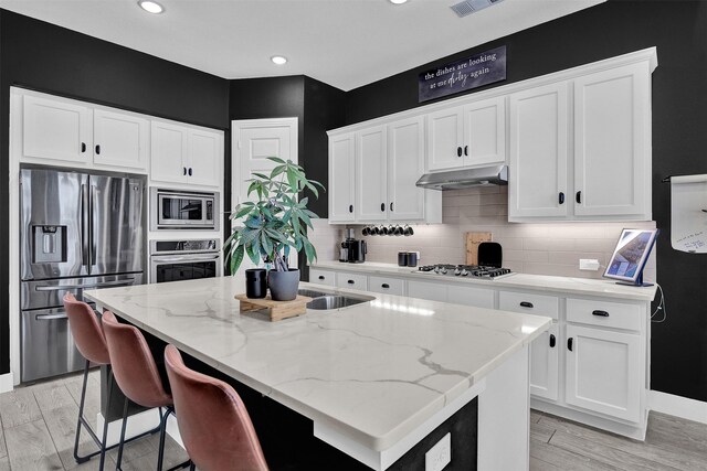 kitchen with white cabinetry, an island with sink, stainless steel appliances, and light stone counters