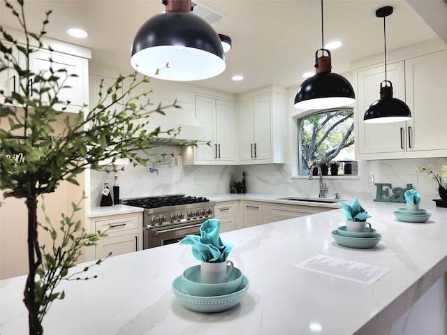 kitchen with sink, white cabinets, light stone counters, and high end stove