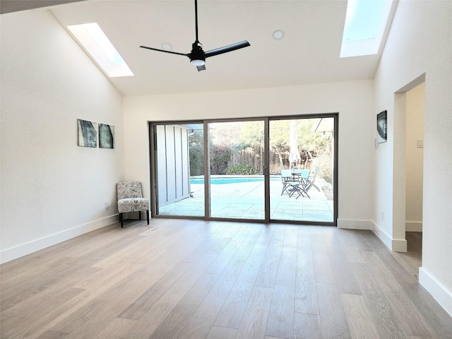 spare room with a skylight, light hardwood / wood-style floors, high vaulted ceiling, and ceiling fan