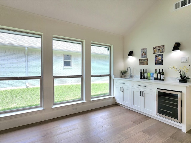 bar with white cabinetry, sink, wine cooler, vaulted ceiling, and light wood-type flooring