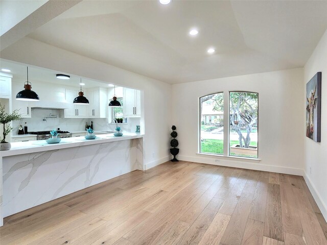 kitchen featuring hanging light fixtures, kitchen peninsula, decorative backsplash, white cabinets, and light wood-type flooring