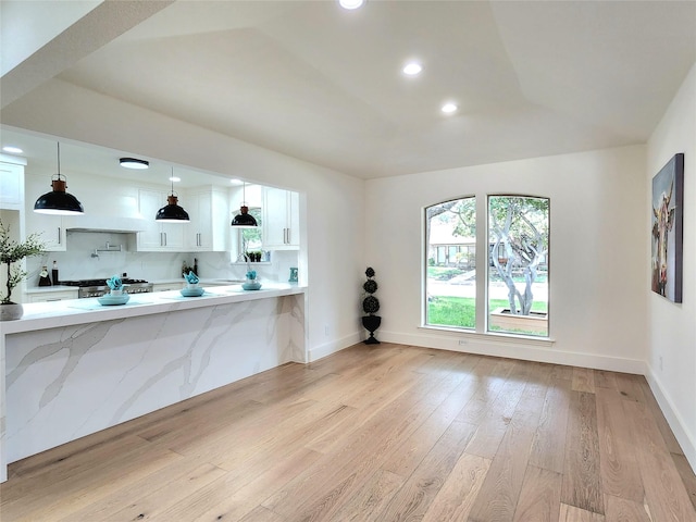 kitchen featuring decorative light fixtures, white cabinets, decorative backsplash, kitchen peninsula, and light hardwood / wood-style flooring