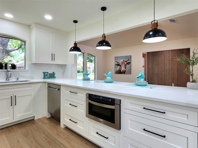 kitchen with sink, hanging light fixtures, light hardwood / wood-style flooring, decorative backsplash, and white cabinetry