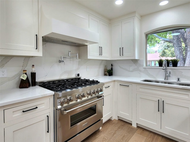 kitchen featuring backsplash, sink, white cabinetry, and high end stainless steel range oven