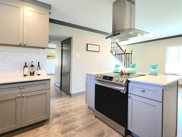 kitchen featuring stainless steel electric stove, island range hood, gray cabinets, and ornamental molding