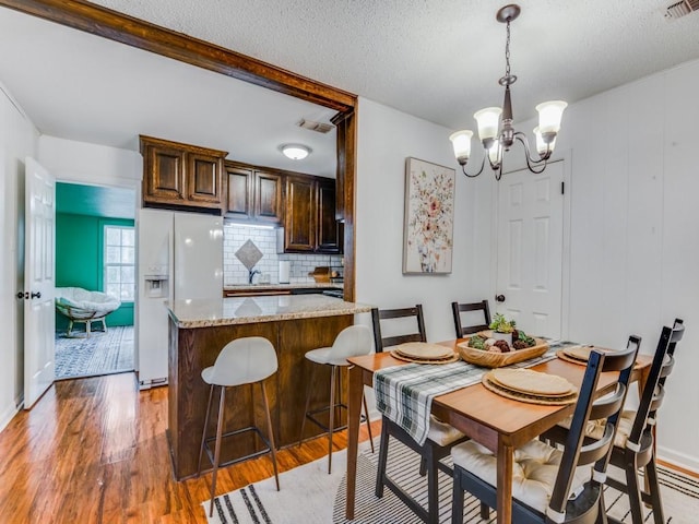 dining space featuring beam ceiling, wood-type flooring, a textured ceiling, and a notable chandelier