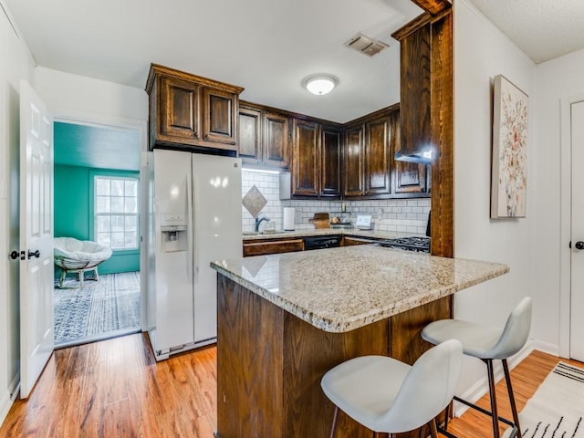 kitchen with light stone countertops, sink, light hardwood / wood-style flooring, white refrigerator with ice dispenser, and backsplash