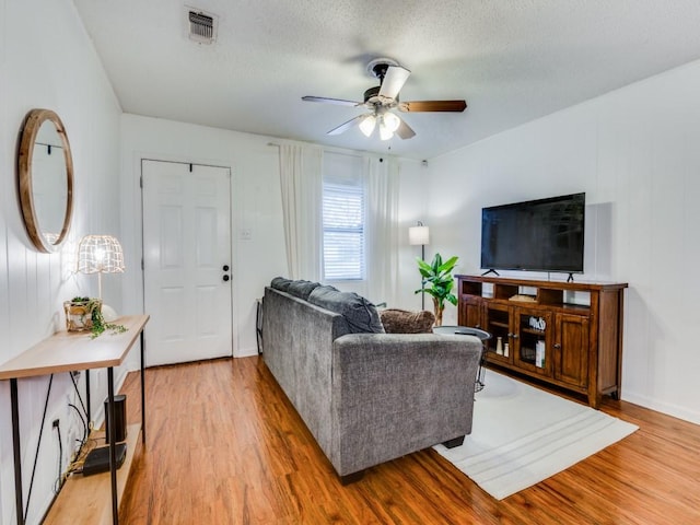 living room with ceiling fan, a textured ceiling, and light wood-type flooring