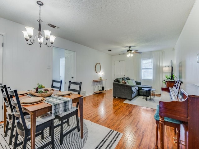 dining area with ceiling fan with notable chandelier, a textured ceiling, and light wood-type flooring